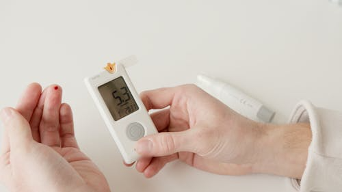 Person measuring blood glucose level using a glucometer during a routine physical exam